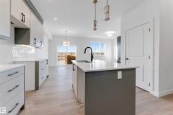 Kitchen featuring hanging light fixtures, an island with sink, tasteful backsplash, light wood-style flooring, and light stone countertops - 