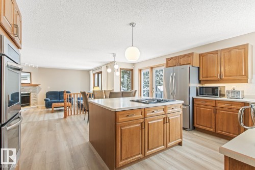 Kitchen with wood finish cabinetry, stainless steel appliances, light wood-style floors, decorative light fixtures, and a textured ceiling - 121 Weaver Drive, Edmonton, AB - Indoor Photo Showing Kitchen