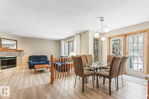 Dining space featuring light wood finished floors, a stone fireplace, and a textured ceiling - 121 Weaver Drive, Edmonton, AB - Indoor Photo Showing Dining Room With Fireplace