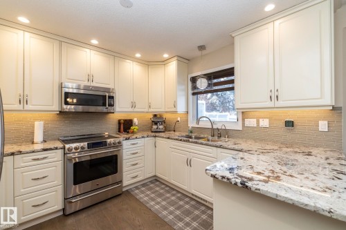 Kitchen featuring stainless steel appliances, white cabinets, light stone countertops, dark wood finished floors, and hanging lights - 932 110A Street, Edmonton, AB - Indoor Photo Showing Kitchen With Double Sink With Upgraded Kitchen