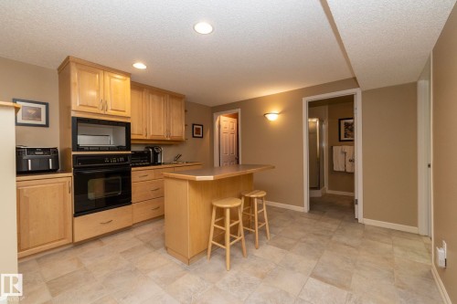 Kitchen featuring a breakfast bar area, black appliances, light wood finish cabinets, a kitchen island, and a textured ceiling - 932 110A Street, Edmonton, AB - Indoor Photo Showing Kitchen