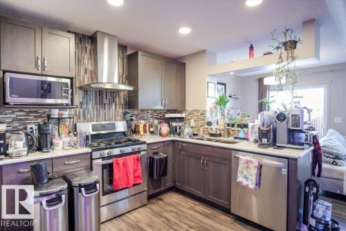 Kitchen with a peninsula, stainless steel appliances, light wood-style flooring, dark wood finish cabinetry, and decorative backsplash - 1426 25 Avenue Nw, Edmonton, AB - Indoor Photo Showing Kitchen With Double Sink