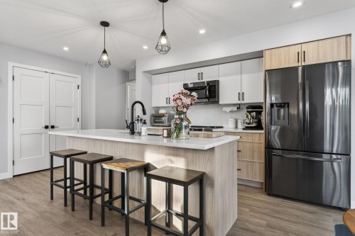 Dual tone kitchen with stainless steel appliances, two tone cabinets, hanging light fixtures, a kitchen bar, and light wood-style floors - 9103 120 Avenue, Edmonton, AB - Indoor Photo Showing Kitchen With Upgraded Kitchen