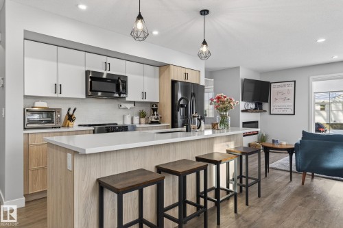Two tone kitchen featuring stainless steel appliances, pendant lighting, a breakfast bar, dark wood-style flooring, and two tone color scheme - 9103 120 Avenue, Edmonton, AB - Indoor Photo Showing Kitchen With Upgraded Kitchen