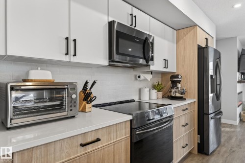 Kitchen featuring stainless steel appliances, tasteful backsplash, light wood finish cabinets, wood finished floors, and modern cabinets - 9103 120 Avenue, Edmonton, AB - Indoor Photo Showing Kitchen With Upgraded Kitchen