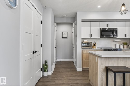 Dual tone kitchen featuring light countertops, stainless steel microwave, backsplash, dark wood-style floors, and pendant lighting - 9103 120 Avenue, Edmonton, AB - Indoor Photo Showing Kitchen