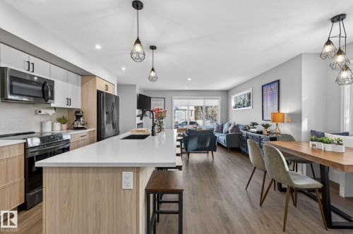 Kitchen featuring stainless steel appliances, open floor plan, a kitchen bar, a center island with sink, and light wood-style floors - 9103 120 Avenue, Edmonton, AB - Indoor