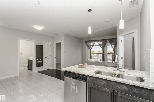 Kitchen with dishwasher, light stone counters, pendant lighting, light tile patterned floors, and dark wood finish cabinetry - 332 5151 Windermere Boulevard, Edmonton, AB - Indoor Photo Showing Kitchen With Double Sink