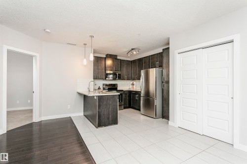 Kitchen featuring stainless steel appliances, dark wood finish cabinets, a peninsula, tasteful backsplash, and pendant lighting - 332 5151 Windermere Boulevard, Edmonton, AB - Indoor Photo Showing Kitchen