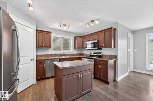 Kitchen with stainless steel appliances, light wood-style floors, a center island, a textured ceiling, and healthy amount of natural light - 2435 Austin Crescent, Edmonton, AB - Indoor Photo Showing Kitchen With Double Sink