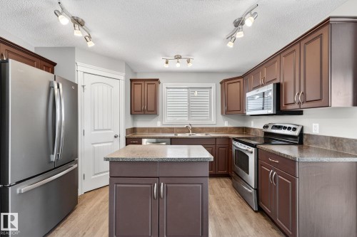 Kitchen featuring stainless steel appliances, a kitchen island, light wood-type flooring, a textured ceiling, and dark wood finish cabinetry - 2435 Austin Crescent, Edmonton, AB - Indoor Photo Showing Kitchen With Double Sink
