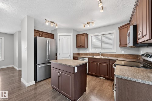 Kitchen with stainless steel appliances, a kitchen island, light wood-style floors, a textured ceiling, and plenty of natural light - 2435 Austin Crescent, Edmonton, AB - Indoor Photo Showing Kitchen With Double Sink