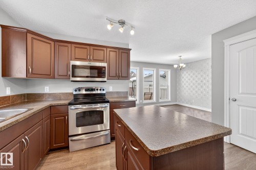 Kitchen with stainless steel appliances, light wood-style floors, a center island, a textured ceiling, and wallpapered walls - 2435 Austin Crescent, Edmonton, AB - Indoor Photo Showing Kitchen