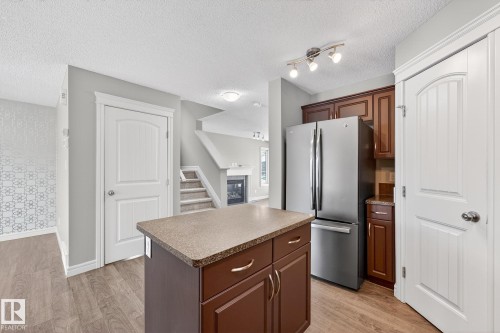 Kitchen featuring freestanding refrigerator, a kitchen island, light wood-type flooring, a textured ceiling, and a glass covered fireplace - 2435 Austin Crescent, Edmonton, AB - Indoor Photo Showing Kitchen