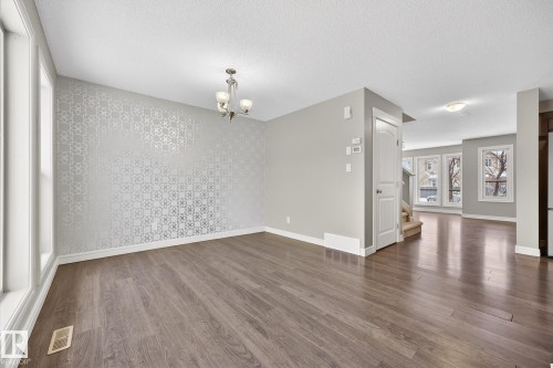 Unfurnished dining area featuring an accent wall, wallpapered walls, wood finished floors, hanging lights, and a textured ceiling - 2435 Austin Crescent, Edmonton, AB - Indoor Photo Showing Other Room