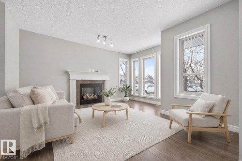 Living area with wood finished floors, a tiled fireplace, a textured ceiling, and track lighting - 2435 Austin Crescent, Edmonton, AB - Indoor Photo Showing Living Room With Fireplace