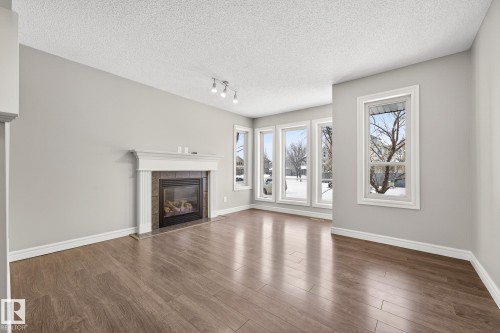 Unfurnished living room with a fireplace, wood finished floors, rail lighting, a textured ceiling, and healthy amount of natural light - 2435 Austin Crescent, Edmonton, AB - Indoor Photo Showing Living Room With Fireplace