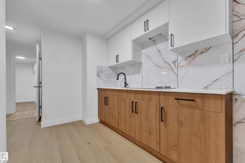 Two tone kitchen featuring two tone color scheme, modern cabinets, light wood-style flooring, backsplash, and light stone countertops - 5504 18 Avenue, Edmonton, AB - Indoor Photo Showing Kitchen