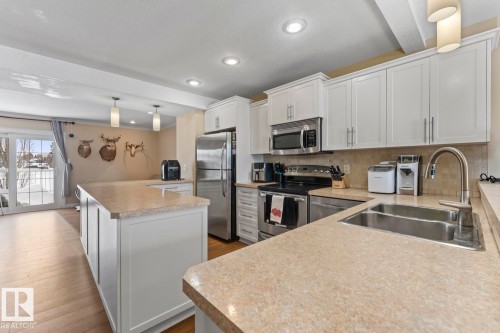 Kitchen featuring hanging light fixtures, white cabinetry, stainless steel appliances, tasteful backsplash, and light countertops - 7 1001 7 Avenue, Cold Lake, AB - Indoor Photo Showing Kitchen With Double Sink With Upgraded Kitchen