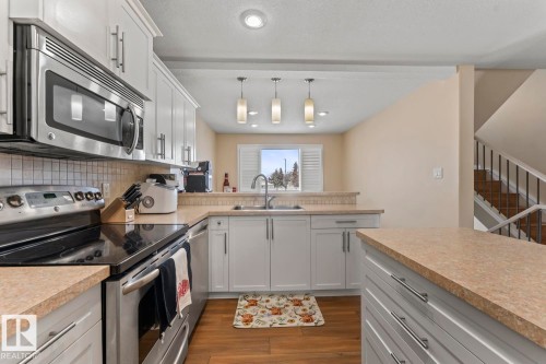 Kitchen with stainless steel appliances, white cabinetry, light countertops, hanging light fixtures, and a textured ceiling - 7 1001 7 Avenue, Cold Lake, AB - Indoor Photo Showing Kitchen With Double Sink