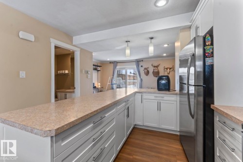 Kitchen featuring white cabinetry, freestanding refrigerator, light countertops, a peninsula, and hanging light fixtures - 7 1001 7 Avenue, Cold Lake, AB - Indoor Photo Showing Kitchen