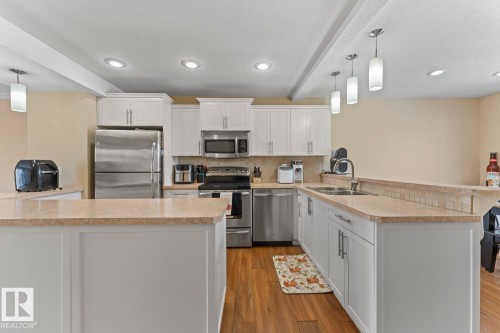 Kitchen featuring pendant lighting, a peninsula, white cabinetry, stainless steel appliances, and beamed ceiling - 7 1001 7 Avenue, Cold Lake, AB - Indoor Photo Showing Kitchen With Double Sink