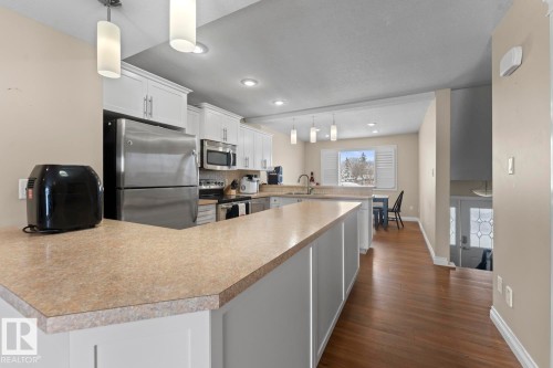 Kitchen featuring a peninsula, white cabinetry, stainless steel appliances, hanging light fixtures, and light countertops - 7 1001 7 Avenue, Cold Lake, AB - Indoor Photo Showing Kitchen With Upgraded Kitchen
