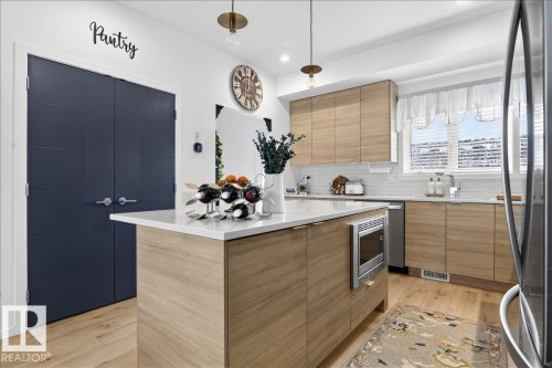 Kitchen featuring stainless steel appliances, modern cabinets, light stone counters, and light wood finished floors - 6609 47 Avenue, Beaumont, AB - Indoor Photo Showing Kitchen