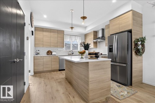 Kitchen featuring stainless steel fridge with ice dispenser, hanging light fixtures, light wood-style flooring, a center island, and light wood finish cabinetry - 6609 47 Avenue, Beaumont, AB - Indoor Photo Showing Kitchen With Upgraded Kitchen