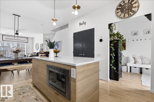 Kitchen featuring modern cabinets, hanging light fixtures, light wood-type flooring, a center island, and stainless steel microwave - 6609 47 Avenue, Beaumont, AB - Indoor With Fireplace