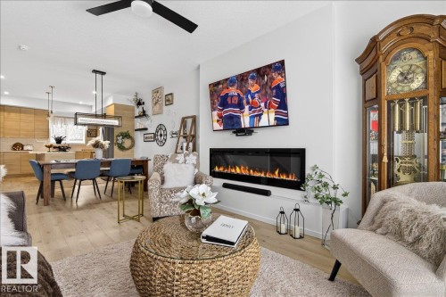 Living area featuring light wood finished floors, a glass covered fireplace, and ceiling fan - 6609 47 Avenue, Beaumont, AB - Indoor Photo Showing Living Room With Fireplace
