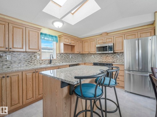 Kitchen with stainless steel appliances, lofted ceiling, light floors, a kitchen island, and a kitchen bar - 151 3400 48 Street, Stony Plain, AB - Indoor Photo Showing Kitchen With Upgraded Kitchen