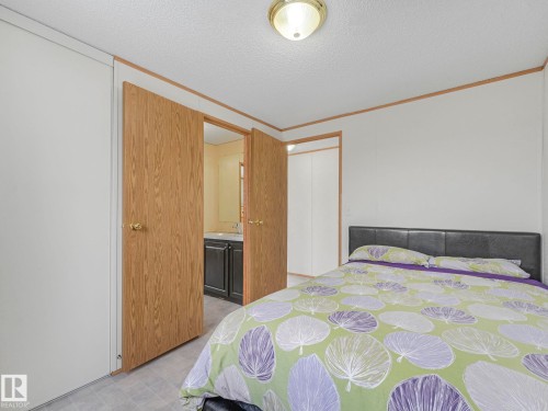 Bedroom with a textured ceiling, ornamental molding, ensuite bathroom, and light floors - 151 3400 48 Street, Stony Plain, AB - Indoor Photo Showing Bedroom