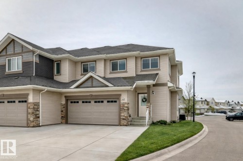 View of front of house with stone siding, driveway, a shingled roof, and an attached garage - 41 4835 Wright Drive, Edmonton, AB - Outdoor With Facade