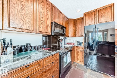 Kitchen featuring dark stone countertops, black appliances, wood finish cabinetry, and light stone finish floors - 777 Butterworth Drive, Edmonton, AB - Indoor Photo Showing Kitchen
