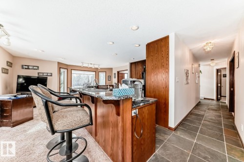 Kitchen featuring wood finish cabinetry, track lighting, a breakfast bar area, dark stone counters, and dark tile patterned flooring - 777 Butterworth Drive, Edmonton, AB - Indoor Photo Showing Other Room
