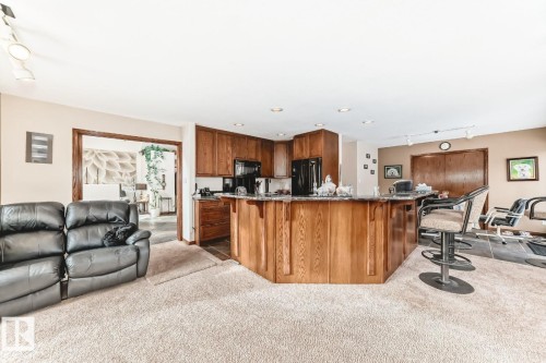 Kitchen featuring open floor plan, rail lighting, a kitchen breakfast bar, light carpet, and black appliances - 777 Butterworth Drive, Edmonton, AB - Indoor