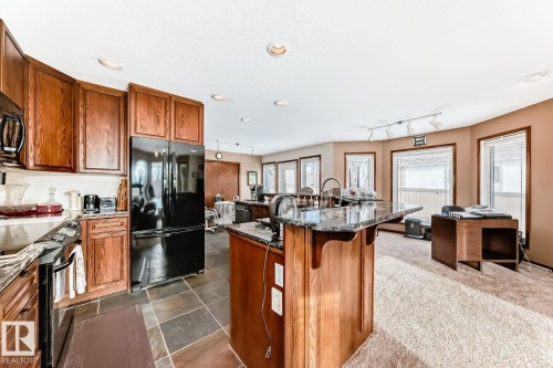 Kitchen featuring wood finish cabinetry, black appliances, dark stone countertops, a breakfast bar, and rail lighting - 777 Butterworth Drive, Edmonton, AB - Indoor Photo Showing Kitchen