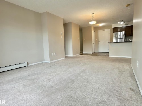 Expansive living area featuring light-toned carpeting and neutral wall paint - 205 11816 22 Avenue, Edmonton, AB - Indoor Photo Showing Other Room