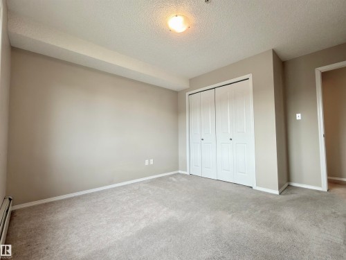 This room features light-colored walls and carpeting, a ceiling-mounted light fixture, and a closet with bi-fold doors - 205 11816 22 Avenue, Edmonton, AB - Indoor Photo Showing Other Room