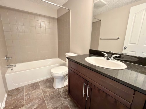The bathroom features a vanity with a dark countertop and an undermount sink, a toilet, and a bathtub with tiled surround - 205 11816 22 Avenue, Edmonton, AB - Indoor Photo Showing Bathroom