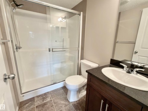 The bathroom features a shower with sliding glass doors, a toilet, a vanity with a dark countertop and an undermount sink. - 205 11816 22 Avenue, Edmonton, AB - Indoor Photo Showing Bathroom