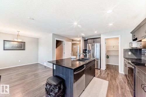 Kitchen featuring an island with sink, stainless steel appliances, light wood finished floors, dark stone counters, and dark wood finish cabinetry - 2823 Duke Crescent, Edmonton, AB - Indoor Photo Showing Kitchen With Double Sink