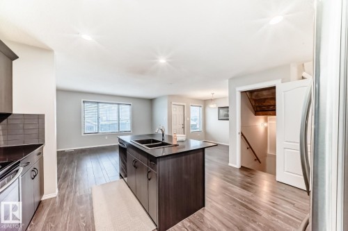Kitchen featuring dark wood finish cabinetry, a center island with sink, light wood-style flooring, decorative light fixtures, and stainless steel appliances - 2823 Duke Crescent, Edmonton, AB - Indoor Photo Showing Kitchen With Double Sink