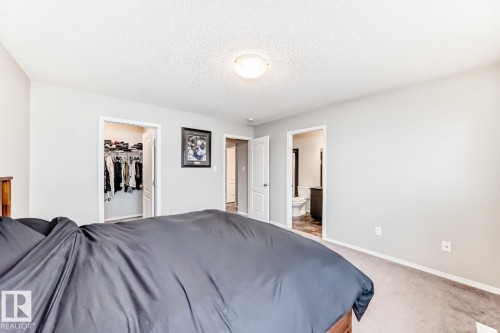 Bedroom with carpet, a spacious closet, a textured ceiling, and ensuite bathroom - 2823 Duke Crescent, Edmonton, AB - Indoor Photo Showing Bedroom