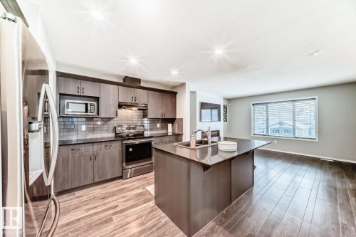 Kitchen with stainless steel appliances, an island with sink, light wood-style flooring, decorative backsplash, and a kitchen bar - 2823 Duke Crescent, Edmonton, AB - Indoor Photo Showing Kitchen With Double Sink With Upgraded Kitchen