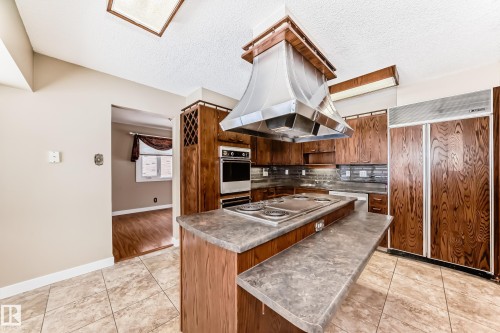 Kitchen with light tile patterned floors, stainless steel appliances, a center island, a textured ceiling, and island exhaust hood - 38 Lancaster Crescent, St. Albert, AB - Indoor Photo Showing Kitchen