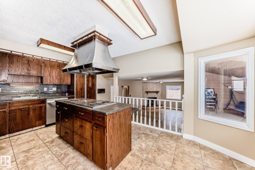 Kitchen featuring light tile patterned floors, dark countertops, a large fireplace, island range hood, and tasteful backsplash - 38 Lancaster Crescent, St. Albert, AB - Indoor Photo Showing Kitchen