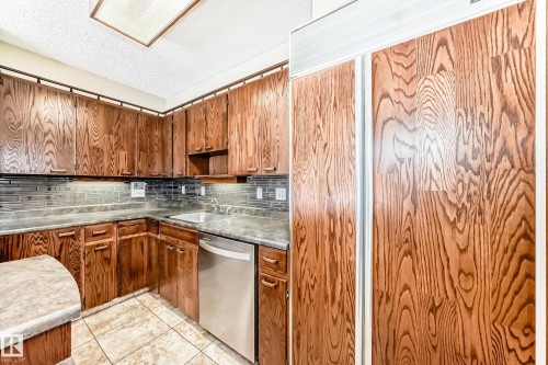 Kitchen featuring a textured ceiling, stainless steel dishwasher, backsplash, light tile patterned floors, and wood finish cabinetry - 38 Lancaster Crescent, St. Albert, AB - Indoor Photo Showing Kitchen