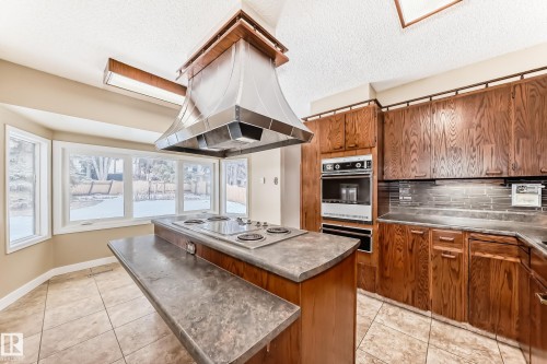 Kitchen with stainless steel countertops, wood finish cabinets, light tile patterned floors, island range hood, and a kitchen island - 38 Lancaster Crescent, St. Albert, AB - Indoor Photo Showing Kitchen With Double Sink